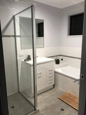 A modern bathroom with a glass shower enclosure, a white sink, a bathtub, and a small window.