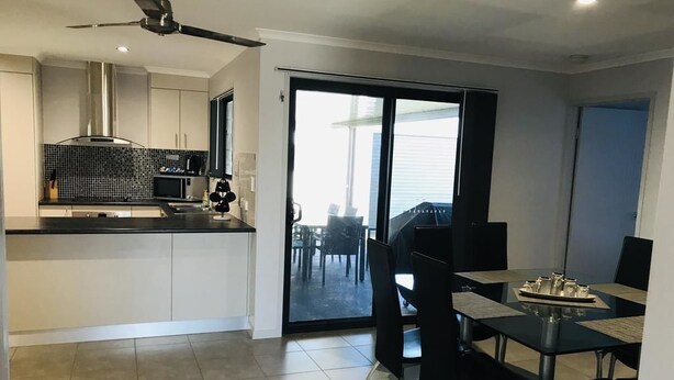 A modern kitchen with a black countertop, stainless steel appliances, and a sliding glass door leading to a balcony. - Hervey Bay Holiday Home (Kawungan)