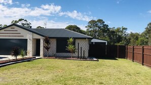 A residential house with a garage, a covered porch, and a fenced backyard. - Hervey Bay Holiday Home (Kawungan)