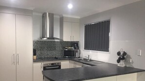 A modern kitchen with white cabinets, a black countertop, a stainless steel range hood, a microwave, and a sink. - Hervey Bay Holiday Home (Kawungan)