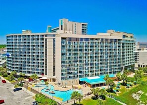Un grand hôtel à plusieurs étages, doté d’une piscine et d’un espace paysager agrémenté de palmiers.