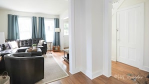 Un salon avec un canapé en cuir foncé, une table basse et un tapis. Une porte donne accès à une autre pièce.