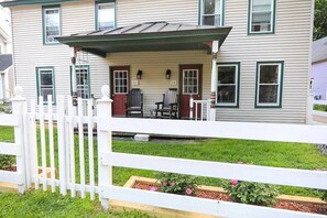 A two-story house with a porch, a white picket fence, and a small garden area with flowers.