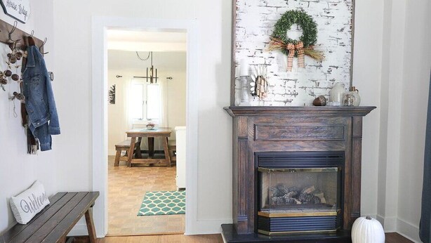 Un salon chaleureux avec une cheminée, un banc, un porte-manteau et une porte donnant sur une autre pièce.