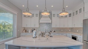 A kitchen with a large island, white cabinets, and pendant lighting.