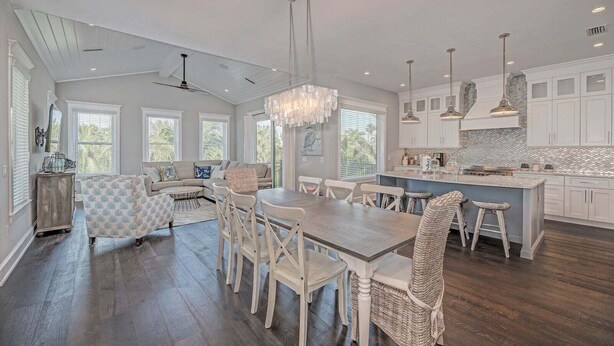 A spacious kitchen with a dining area, large windows, and a chandelier.
