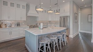 A modern kitchen with white cabinets, a large island with bar stools, stainless steel appliances, and pendant lighting.