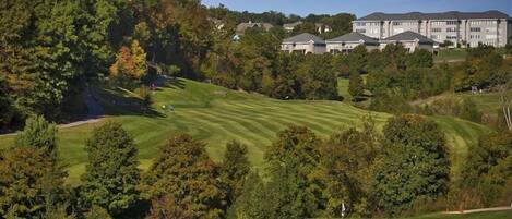 Un campo de golf con un club de campo y edificios residenciales al fondo.