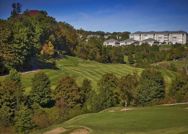 Un campo de golf con un club de campo y edificios residenciales al fondo.