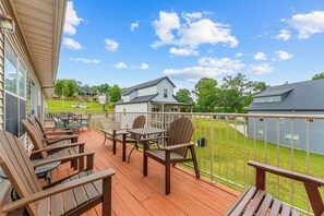 Une terrasse en bois avec des meubles d’extérieur, une vue dégagée sur un quartier résidentiel et un ciel bleu avec des nuages.