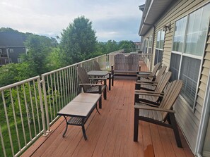 A wooden deck with outdoor furniture, a railing, and a view of greenery and buildings.