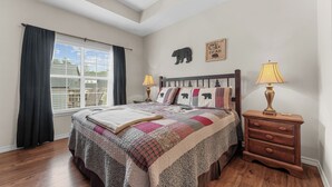 Een slaapkamer met een groot bed, twee nachtkastjes met lampen, een raam met gordijnen, een plafondventilator en een beren-thema decoratie aan de muur.