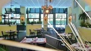 A restaurant with tables and chairs, large windows, and hanging lights.