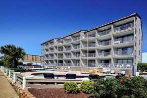 A multi-story hotel with balconies, a swimming pool, and lounge chairs.