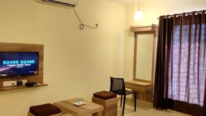 Une chambre d’hôtel équipée d’un téléviseur fixé au mur, d’une petite table avec une chaise, d’un miroir et d’une fenêtre avec des rideaux.
