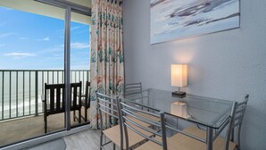 A balcony with a glass table and chairs, a view of the beach, and a painting on the wall. - Direct Oceanfront Studio On The Golden Mile (Myrtle Beach)