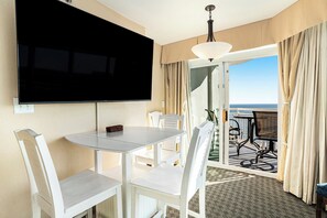Ein Hotelzimmer mit einem wandmontierten Flachbildfernseher, einem Esstisch mit Stühlen und einem Balkon mit Meerblick.