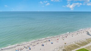 A beach with people and umbrellas, a clear sky, and calm water. - Amazing Views 30 ft. balcony 1 bedroom Myrtle Beach (Myrtle Beach)