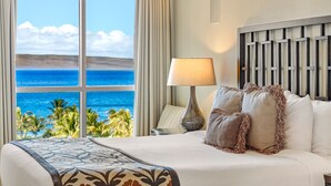 Une chambre d’hôtel avec un grand lit, une vue sur l’océan, une lampe et une tête de lit.