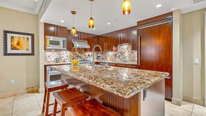 Une cuisine moderne dotée d’un grand îlot central, de meubles en bois, d’appareils électroménagers en acier inoxydable et de luminaires suspendus.