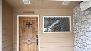 Une porte en bois surmontée d’une fenêtre à grilles métalliques, un revêtement extérieur de couleur beige et un mur en pierre.