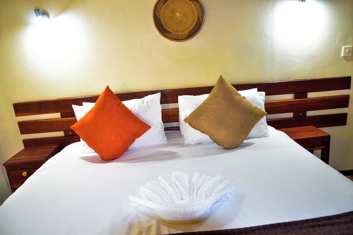 A neatly made bed with white linens, two pillows (one orange, one brown), and a white decorative item on the bed.