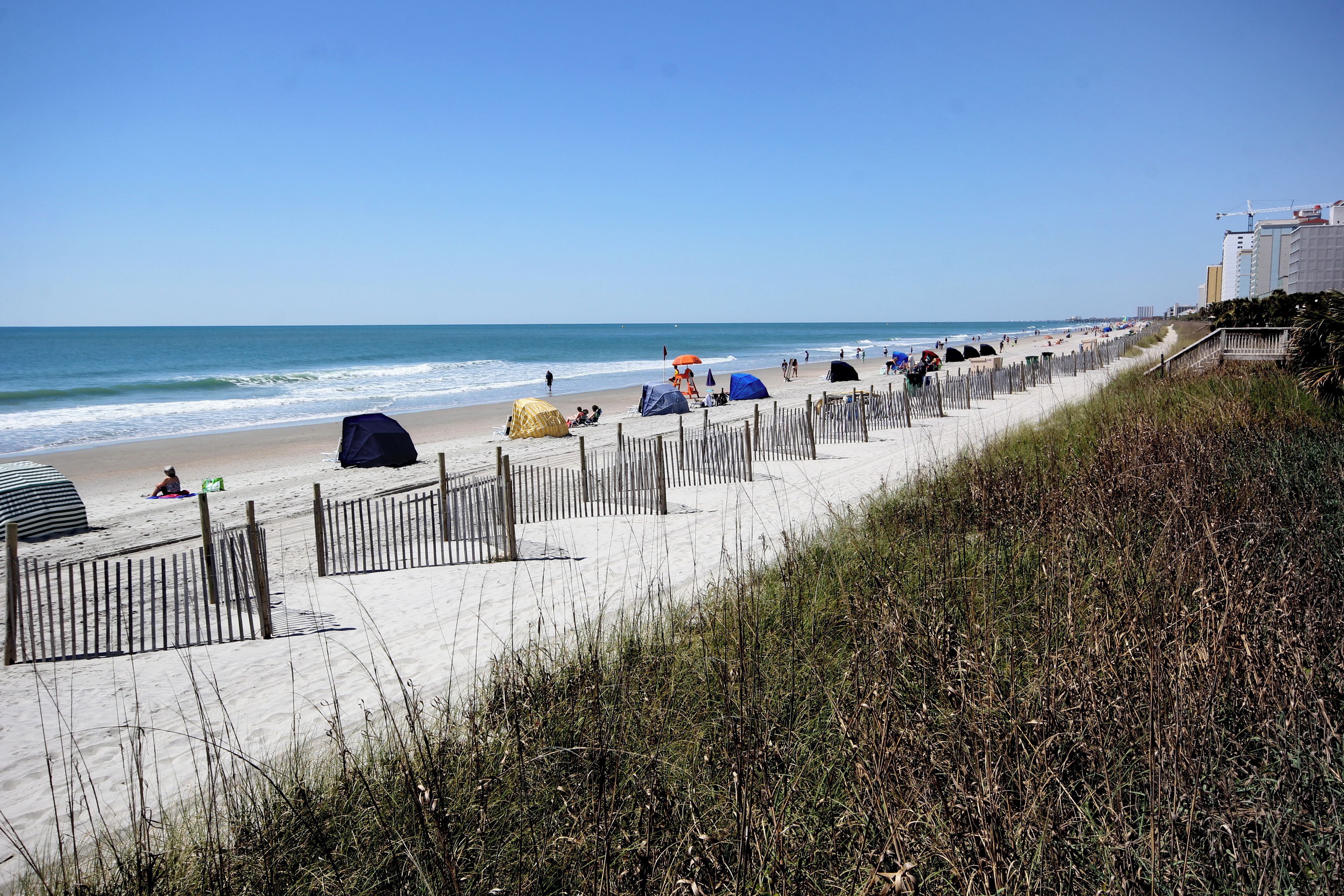 A beach with tents and a wooden fence along the shore.