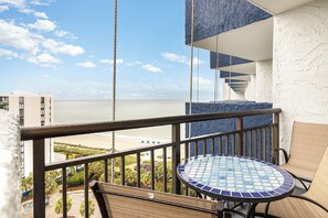 Een balkon met uitzicht op het strand, een ronde tafel en een stoel.