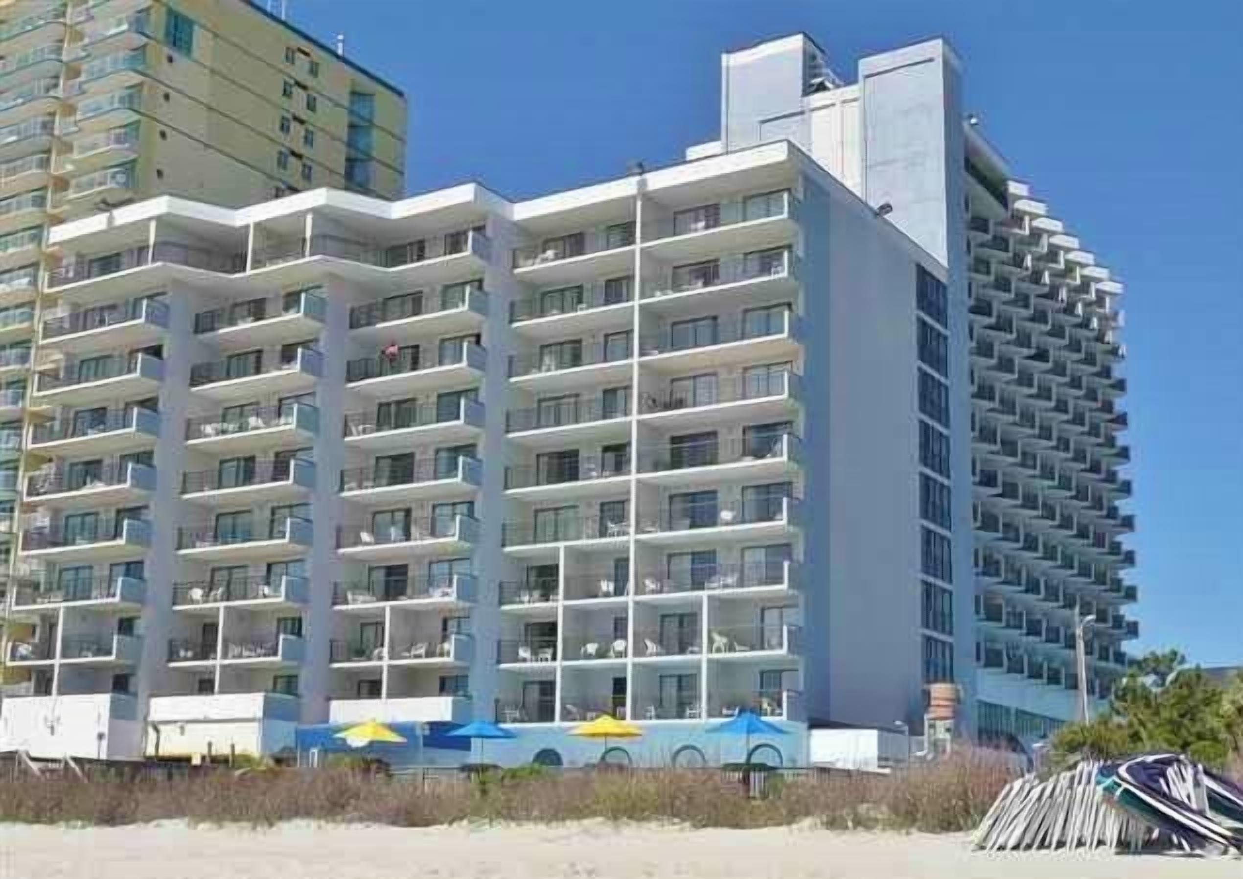A multi-story hotel with balconies, a pool area, and a beachside location.