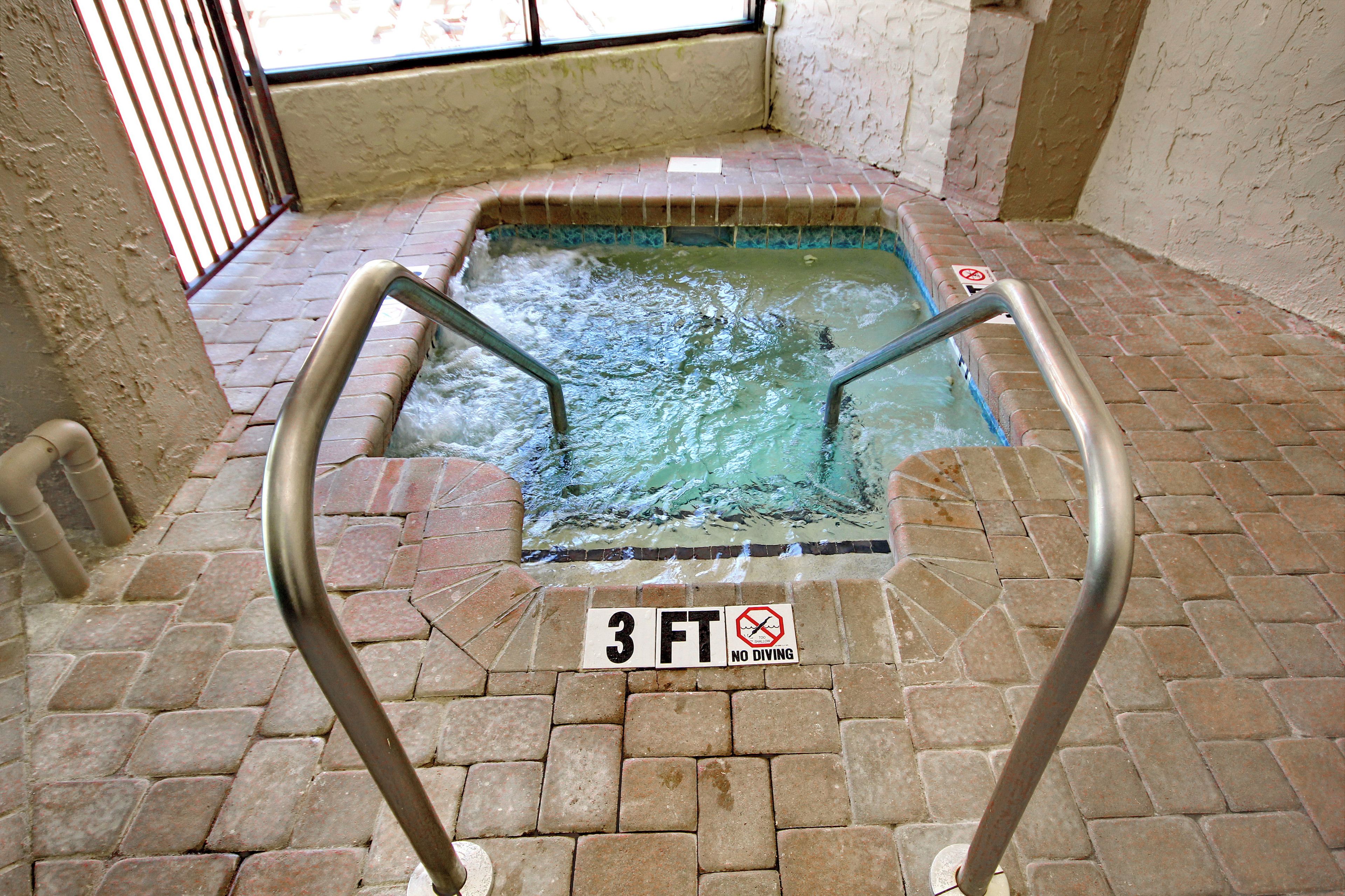 A 3-foot deep hot tub with a no diving sign, surrounded by a brick floor and a metal safety railing.