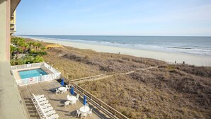 A beach view from a balcony with a pool and outdoor seating.