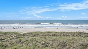 A beach with people walking and sitting, a sandy shore, and the ocean.