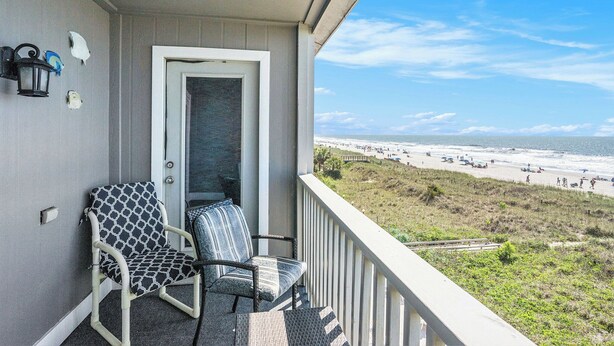 A balcony with two chairs, a door, and a view of the beach.