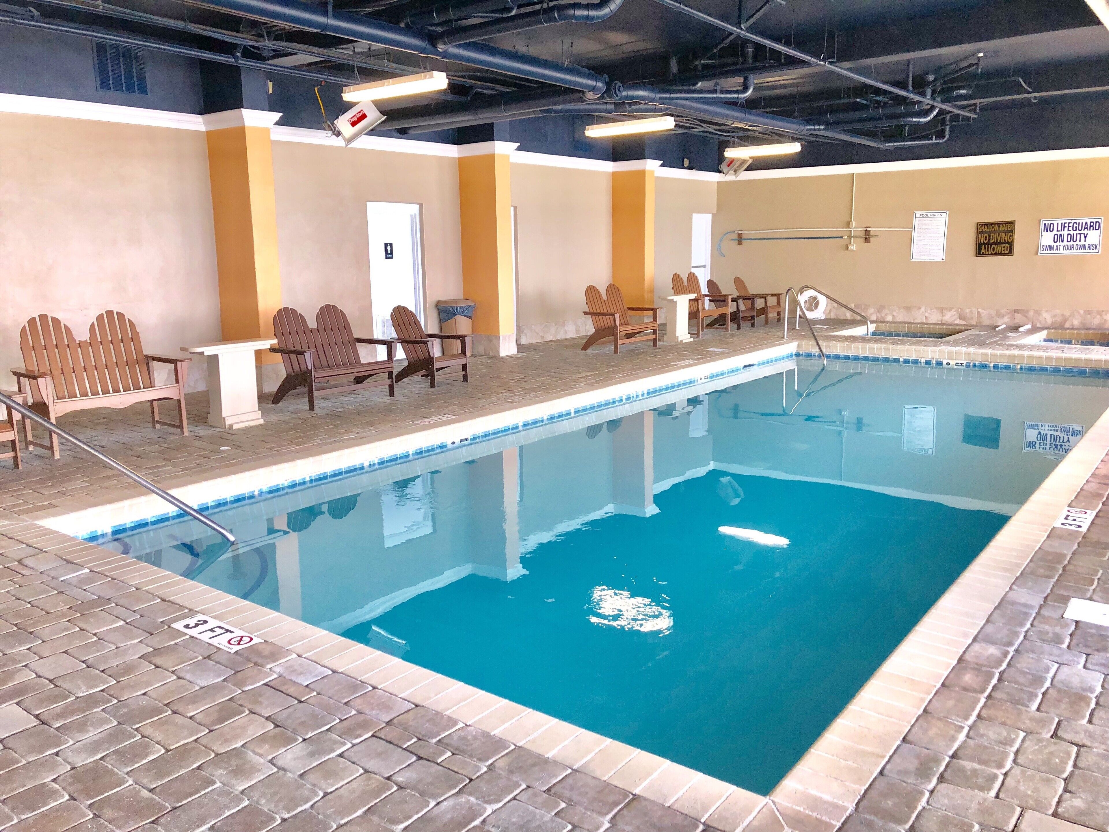 Une piscine intérieure avec un sol carrelé, des chaises en bois et un poste de surveillance pour les sauveteurs.
