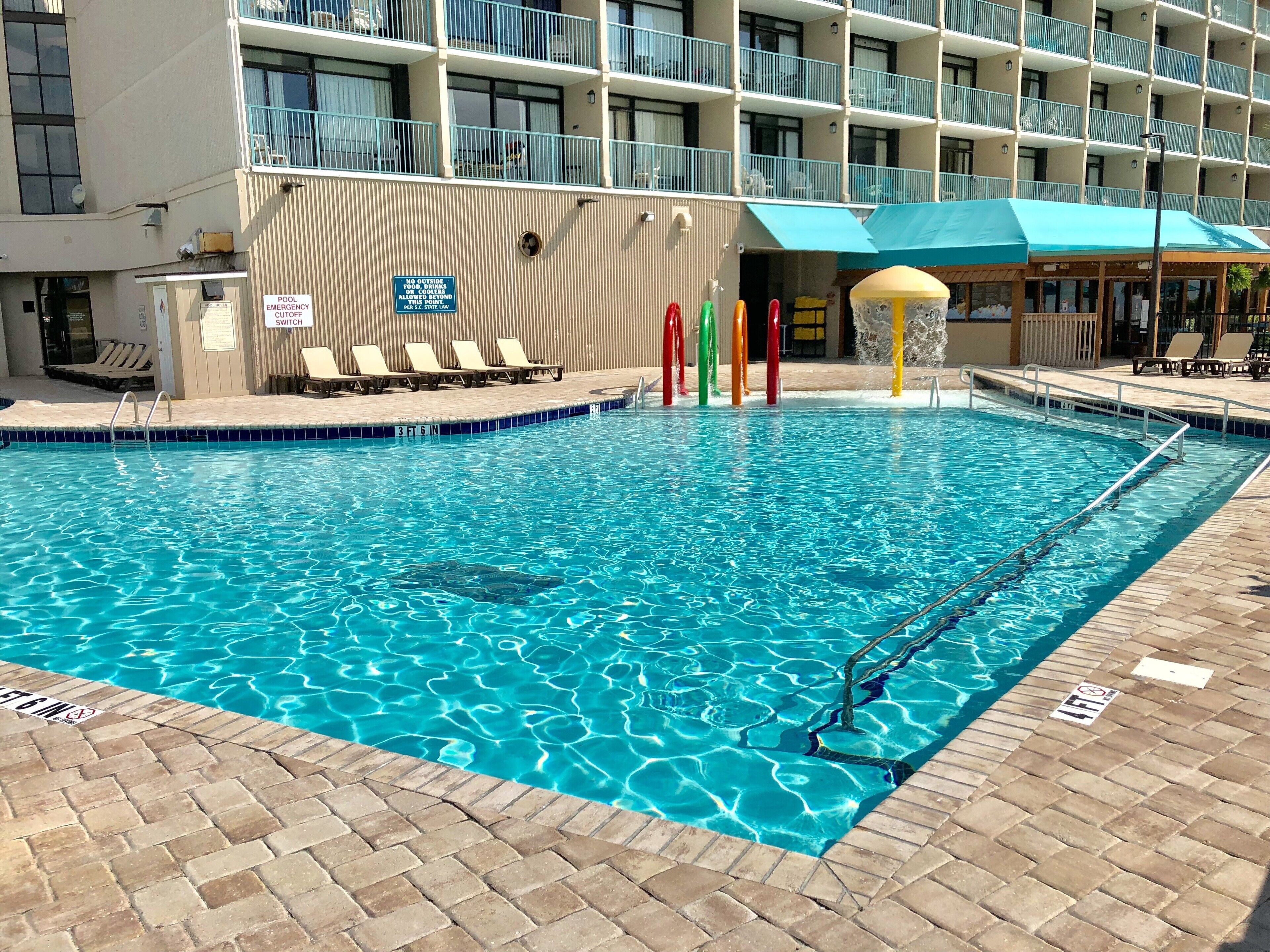 A swimming pool with a tiled edge, a pool switch sign, and a no outside emergency cutoff sign.