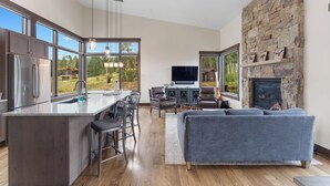 A modern kitchen with a large island, dining area, and a stone fireplace. - Spacious Mountain Home, Panoramic View from Private Balcony, Central Location (Silverthorne)