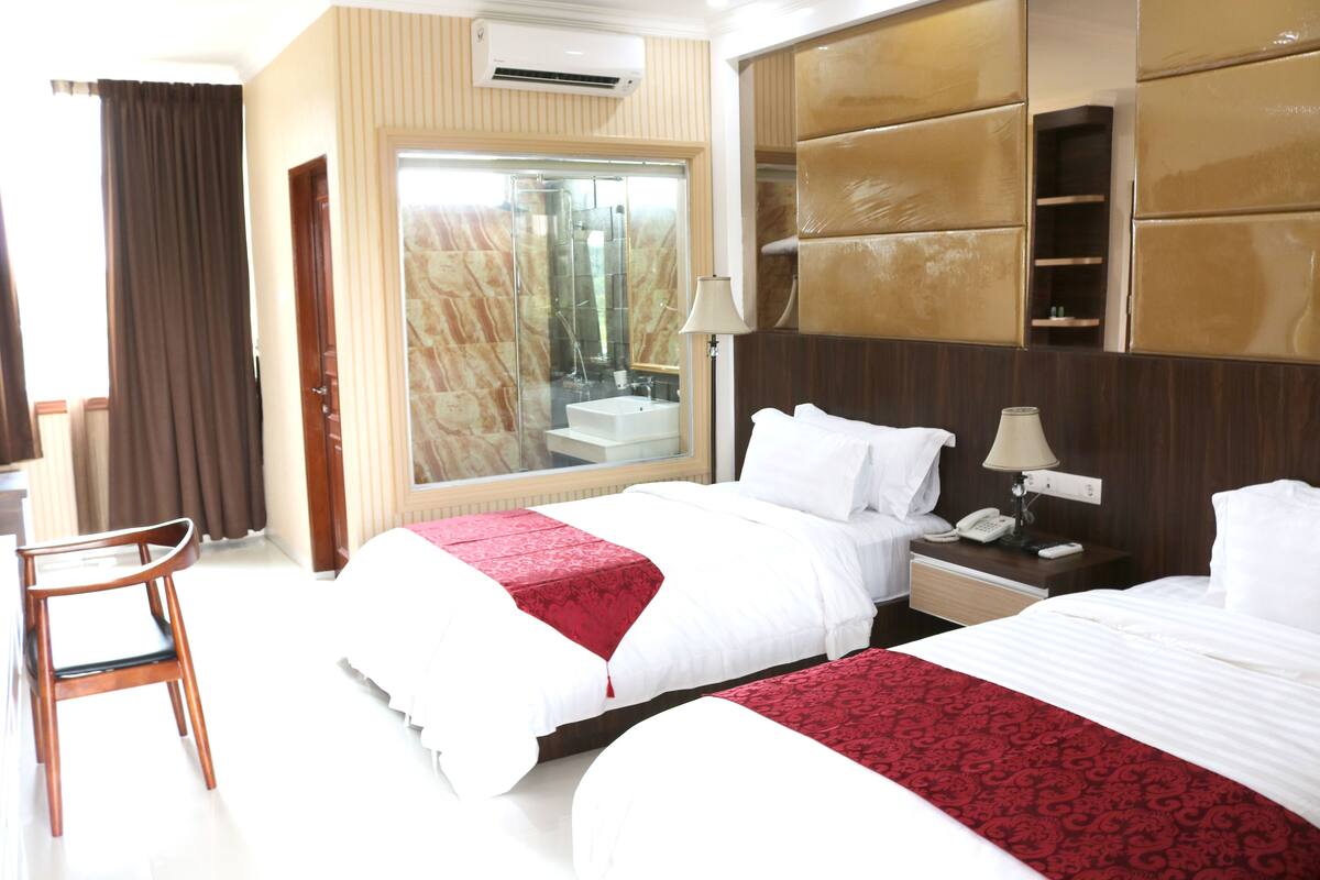 A hotel room with two beds, a desk, a chair, a bathroom with a large mirror, and a wardrobe.