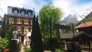 A hotel with a traditional European facade, a sign indicating it is open, and a view of mountains in the background. - Hôtel du Clocher (Chamonix-Mont-Blanc)