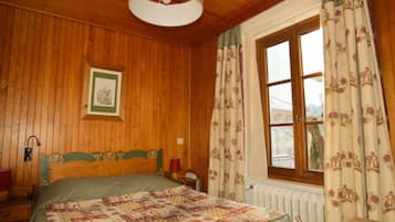 Un dormitorio con paneles de madera, una cama, una mesita de noche, una mesa y una ventana con cortinas.
