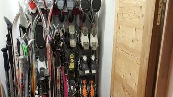 Un couloir étroit, avec une porte en bois sur la droite et des paires de skis et de snowboards sur la gauche.