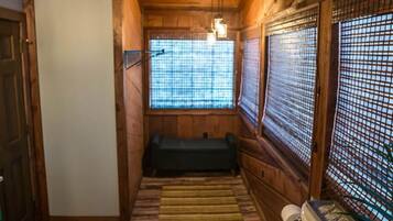 Une salle de bain rustique, aménagée dans une cabane en bois, avec des toilettes, un banc et un ventilateur de plafond.