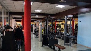 Un gimnasio con diferentes máquinas de ejercicio, un pilar rojo y un banco.