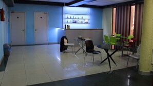 Un hall con pared azul, un mostrador de recepción, un extintor y una zona de estar con sillas y una mesa.