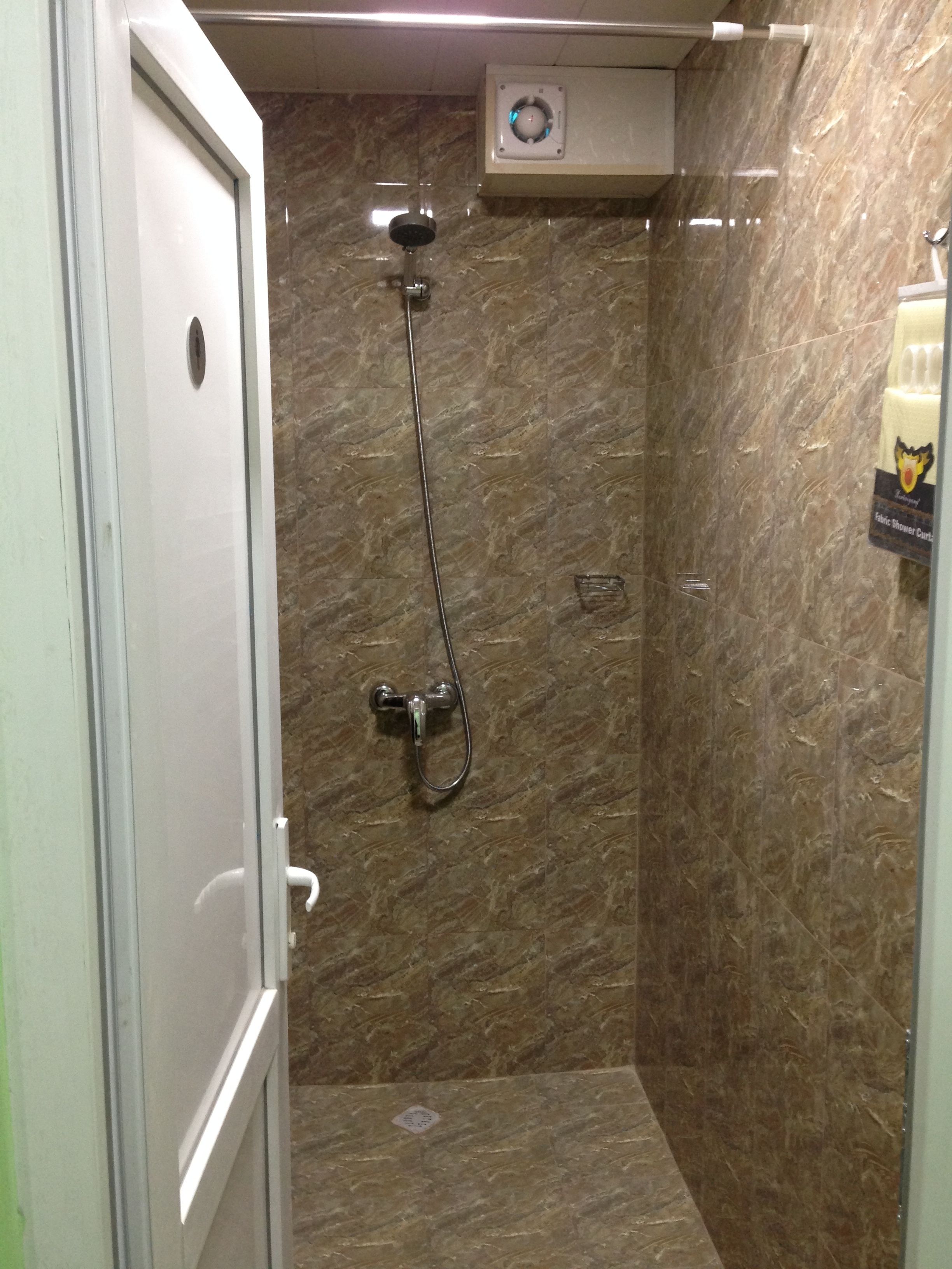 A bathroom with a shower, marble walls, and a hand dryer.