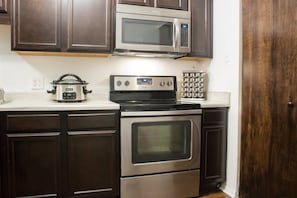 A kitchen with dark wood cabinets, a stainless steel microwave, a built-in oven, and a slow cooker.