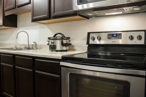 A kitchen with dark wooden cabinets, a stainless steel sink, a built-in microwave, and a Whirlpool stove. - Exclusive Private Room (Raleigh)