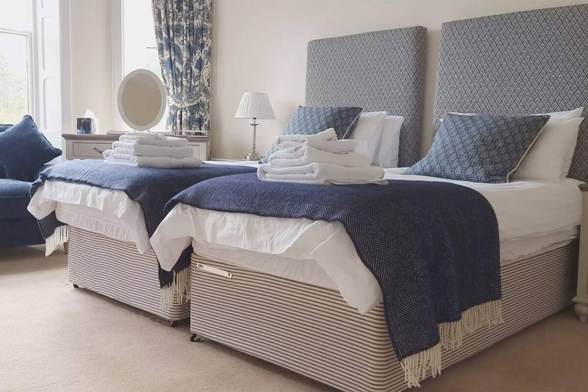 A bedroom with two beds, a sofa, a bedside table with a lamp, and a mirror.