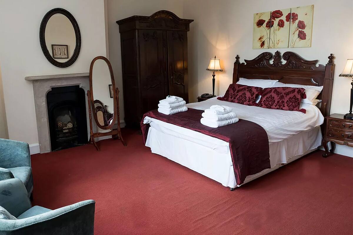 A bedroom with a large bed, a wooden wardrobe, a fireplace, and a chair.