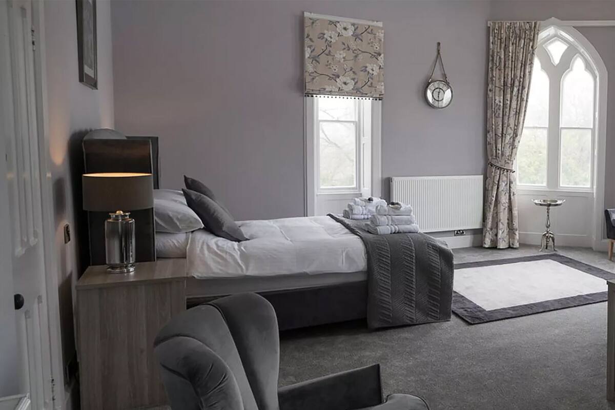 A modern bedroom with a bed, bedside table, lamp, and a view of the outside through a window.