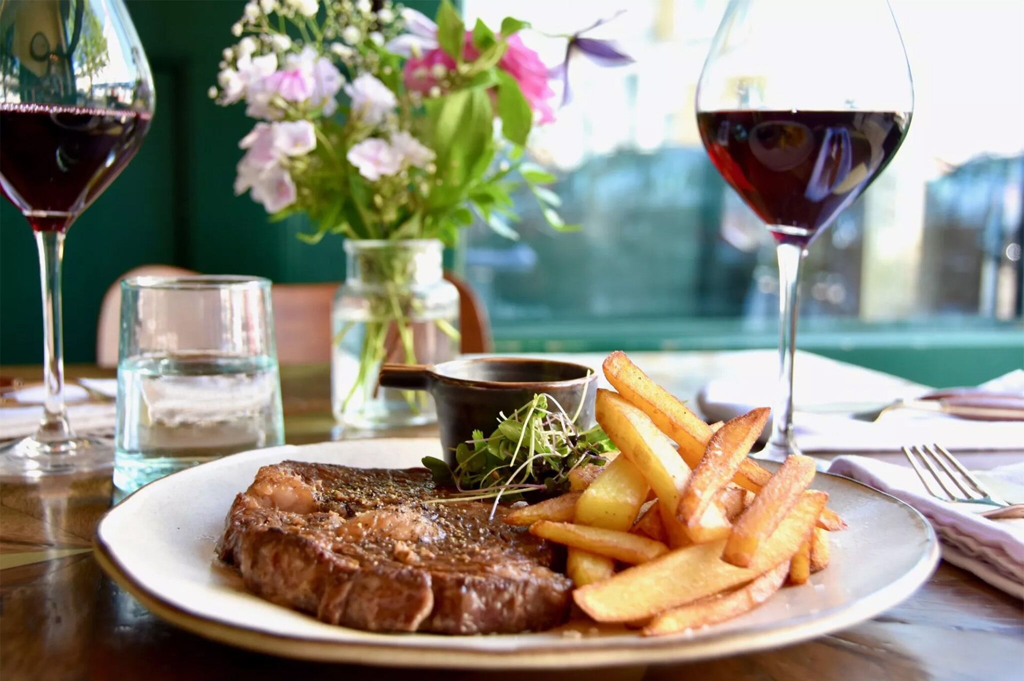 A plate with steak and fries, a glass of red wine, and a vase with flowers on a table.